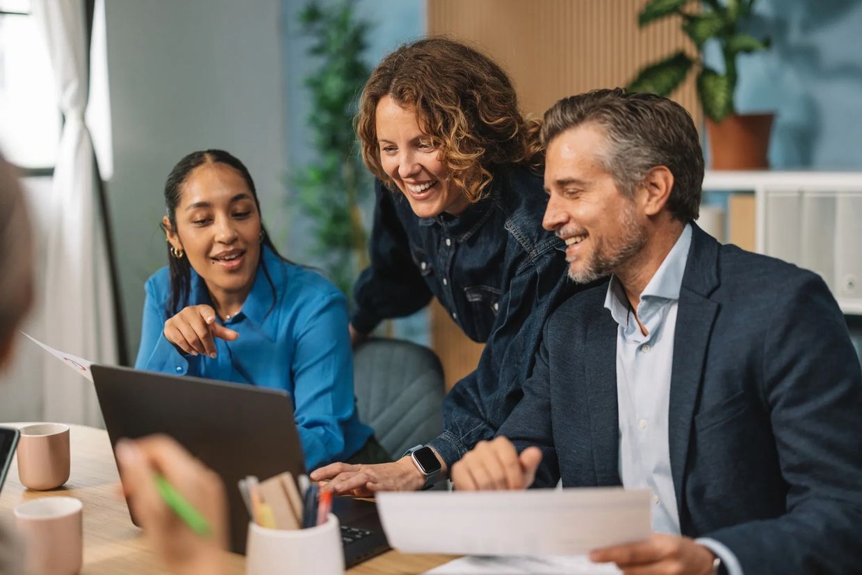 Three colleagues happily working together on a laptop.