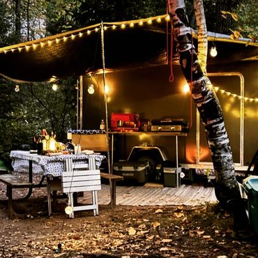 Cozy outdoor camping setup with string lights and a picnic table at dusk.