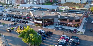 A bustling shopping center with various shops and a crowded parking lot under clear daylight.