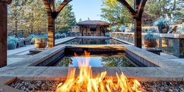 Outdoor pool area with fire feature and shaded seating under wooden beams.