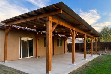 Wooden patio cover with string lights over a concrete slab beside a house.