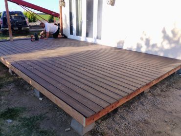Newly built wooden deck attached to a house with a person working nearby.