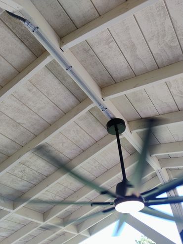 Spinning ceiling fan mounted on a wooden ceiling with beams.