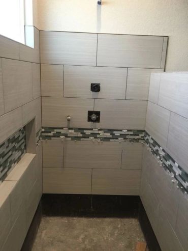 Partially tiled shower area with decorative tile strip and plumbing fixtures.