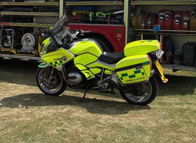 Bright yellow ambulance motorcycle parked on grass.