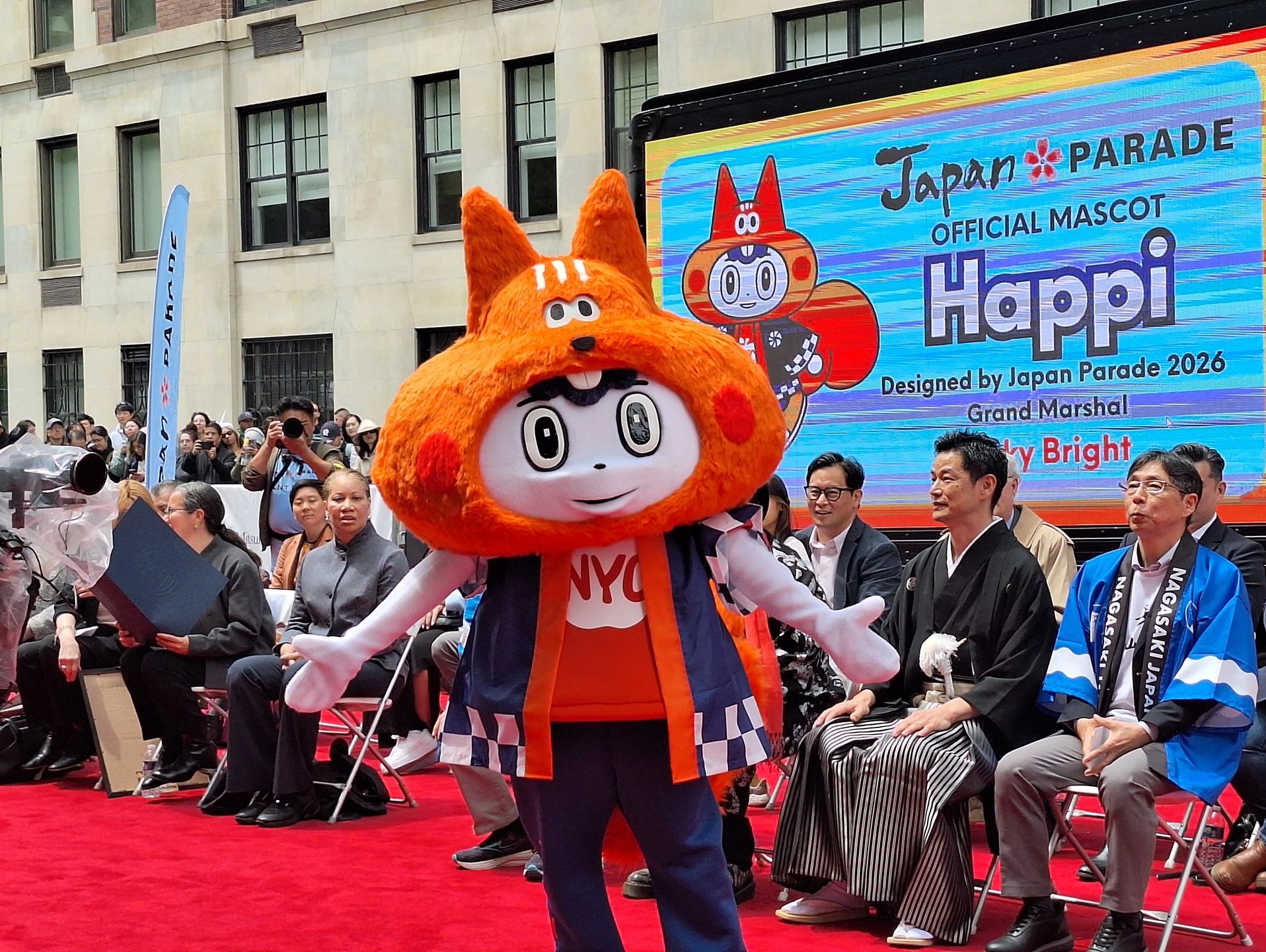 Happi, the official mascot of the Japan Parade, posing on a red carpet with spectators.