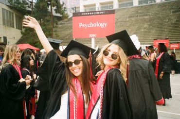 Two female graduates celebrating at psychology commencement.