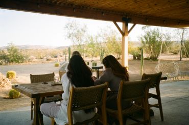 Three people sitting under a covered patio overlooking a desert landscape.