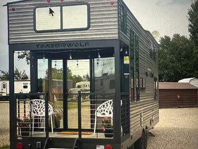 Compact Timberwolf camper trailer with a small porch and white chairs.