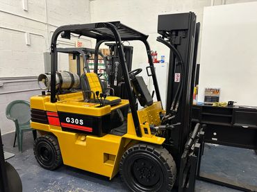 Yellow Toyota G30S forklift parked indoors beside office furniture.