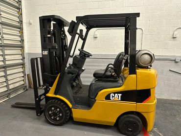 Yellow CAT forklift parked indoors with propane tank attached.