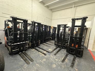 A row of parked forklifts inside a warehouse with white walls.