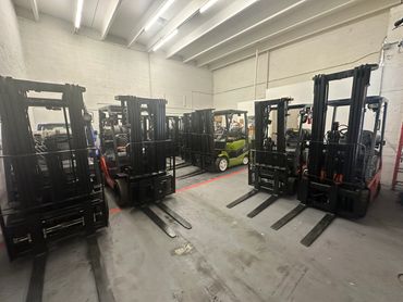 A row of forklifts parked inside a warehouse with bright ceiling lights.