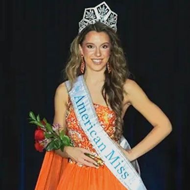In an orange gown, American Miss National Jr Teen is wearing her new AMP National crown & banner.