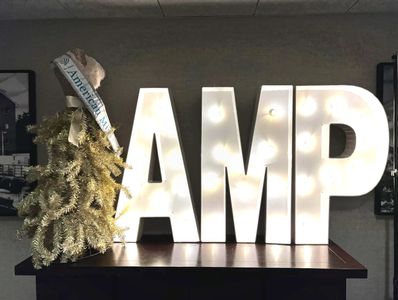 American Miss Pageant letters in lights AMP and a gown fake tree in gold with the AMP banner.