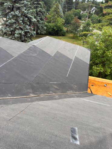 Newly installed roofing underlayment on a house roof with trees in the background.