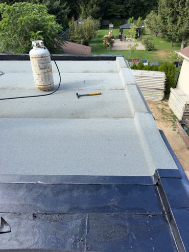 Flat roof with propane tank and hammer, overlooking a garden with trees and a gazebo.