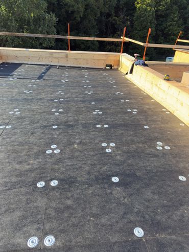 A flat roof under construction with black waterproofing material and wooden edges.