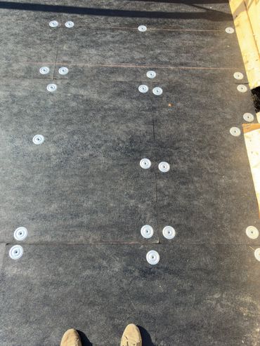 Black roofing underlayment with white fasteners on a wooden deck.