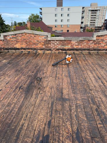 Leaf blower on a weathered wooden rooftop with brick wall.