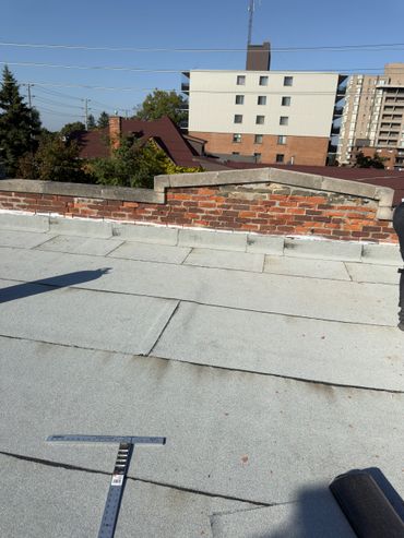 Rooftop view with brick wall and nearby buildings under clear blue sky.