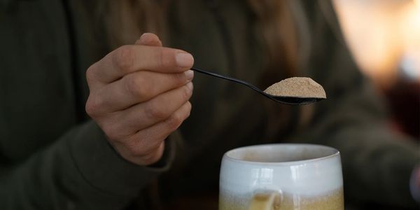 Person adding a spoonful of high quality lion's mane mushroom powder to their daily coffee or tea