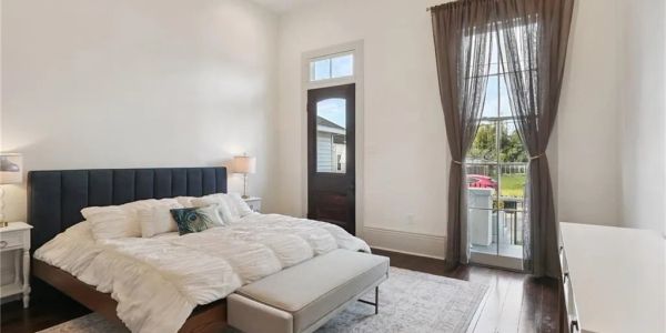 Bright bedroom with a large bed, bench, and door leading outside.