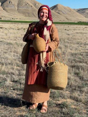 Woman in traditional attire holding pottery and baskets in a field.