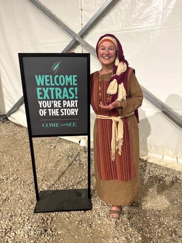 Woman in traditional attire smiling next to welcome sign.