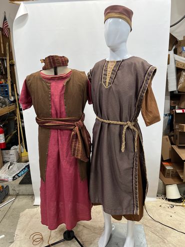 Two mannequins display traditional, colorful robes with belts in a workshop setting.