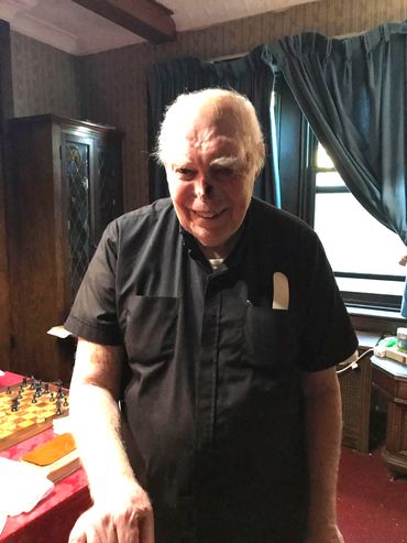 Msgr. Philip Reilly in his dining room. Here he had his chess board, his cockatiel, B.J. a small TV
