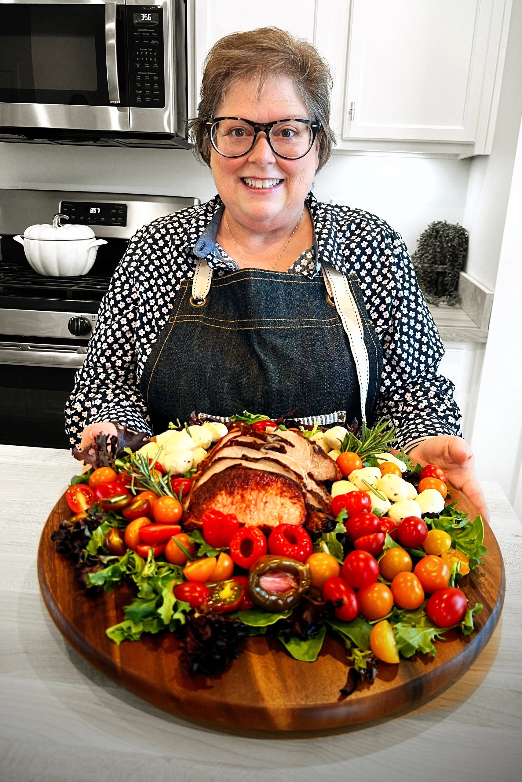 Lorene is in the kitchen showing off a dinner board with a pork roast and Italian veggies.