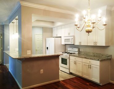 Bright kitchen with white cabinets, granite countertops, and a golden chandelier.