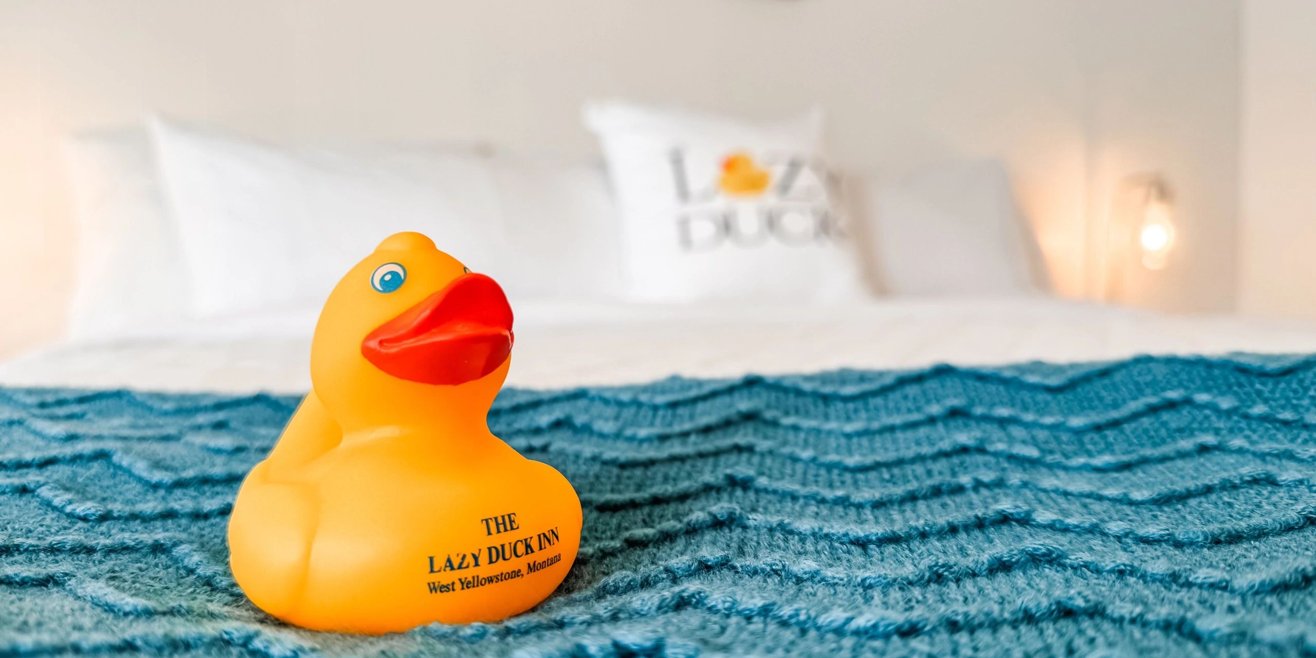 A yellow rubber duck with red beak on a blue textured blanket on a bed.