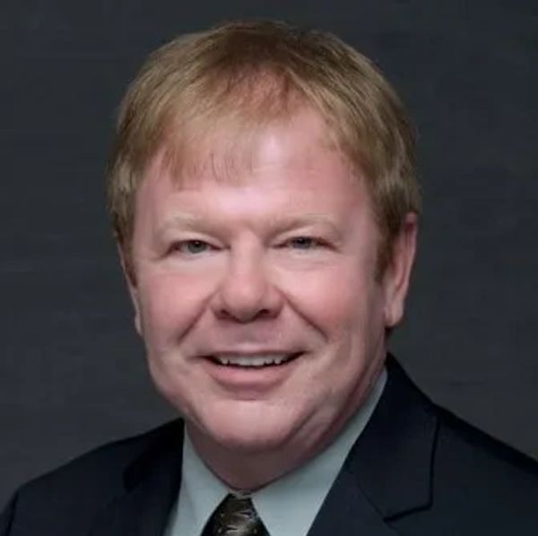 Smiling man in a suit against a dark background.