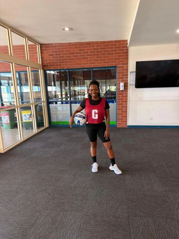 A woman in sportswear holding a netball indoors.