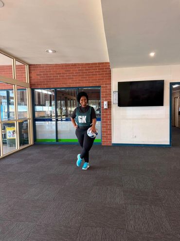 A smiling woman in sportswear holding a netball indoors.