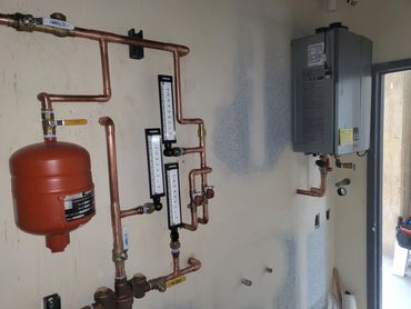 Copper pipe system with gauges and a water heater mounted on a wall.