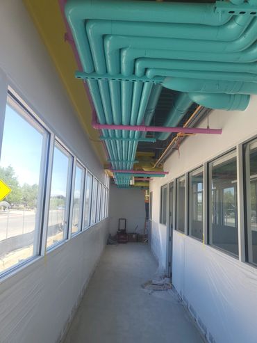 Colorful teal and purple pipes run along the ceiling of a bright hallway under construction.