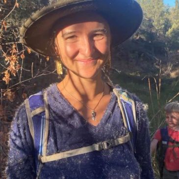 Smiling woman in hiking gear and hat outdoors.