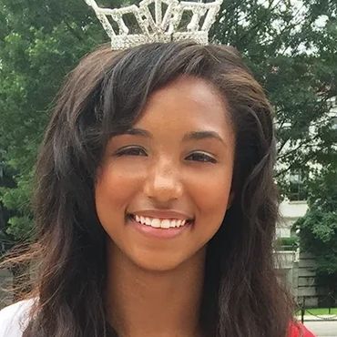 Smiling young woman wearing a sparkling crown outdoors.