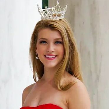 Young woman wearing a crown and red strapless dress smiling.