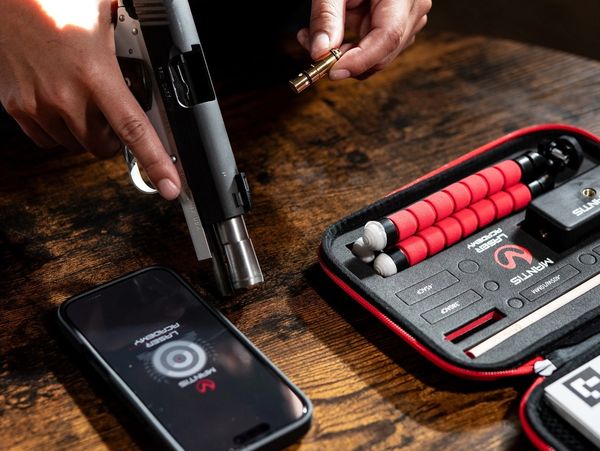 Person loading a bullet into a handgun on a wooden table with shooting accessories.