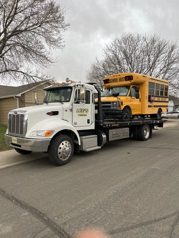 A white tow truck carrying a yellow school bus on a residential street.