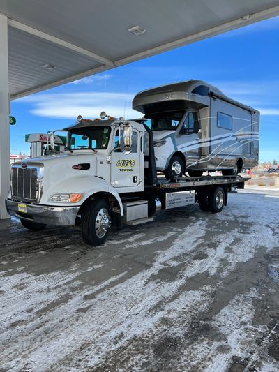 A tow truck from Lee's Towing carrying a damaged RV at a gas station.