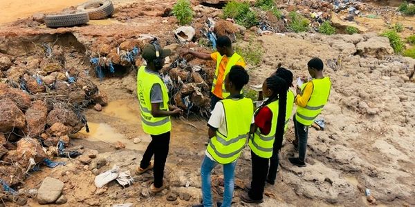 Group in reflective vests inspects a muddy, rocky site outdoors.