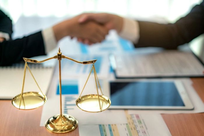 Golden scales of justice with two people shaking hands in the background.