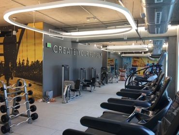 Commercial gym with various equipment and overhead ambient lighting in creative shapes.