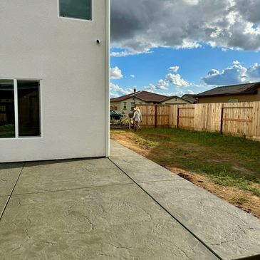 Newly poured concrete patio beside a house with workers in the background.