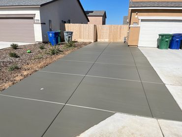 Newly paved concrete driveway between two houses under a clear blue sky.